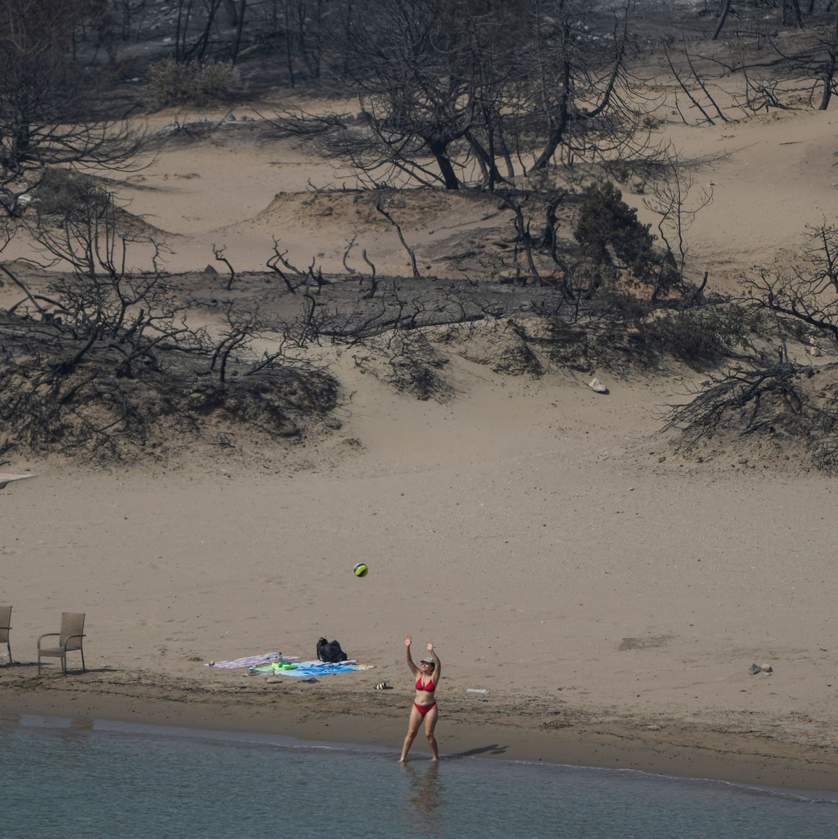 Hinten die verbrannte Vegetation, vor das Mittelmeer. Eine Frau spielt mit einem Ball am Strand bei Gennadi auf Rhodos. - Foto: Petros Giannakouris/AP