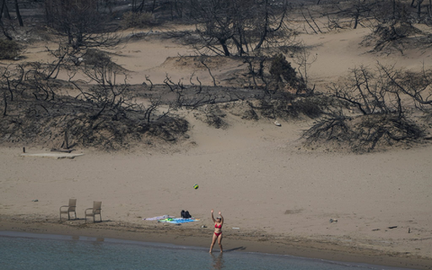 Hinten die verbrannte Vegetation, vor das Mittelmeer. Eine Frau spielt mit einem Ball am Strand bei Gennadi auf Rhodos. - Foto: Petros Giannakouris/AP