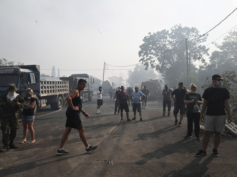 Verunsicherte Anwohner auf einer Straße in Nea Anchialos. Wegen der starken Rauchbildung flüchteten viele Urlauber an den örtlichen Strand. - Foto: Tatiana Bolari/Eurokinissi/AP/dpa