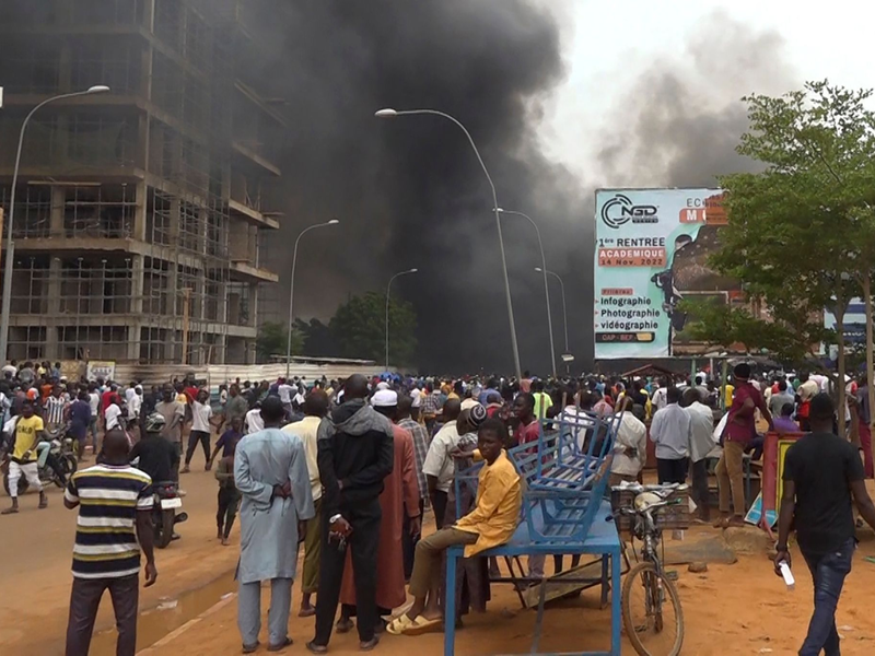Mit dem brennenden Hauptquartier der Regierungspartei im Rücken demonstrieren Anhänger meuternder Soldaten in der Hauptstadt Niamey. - Foto: Fatahoulaye Hassane Midou/AP/dpa