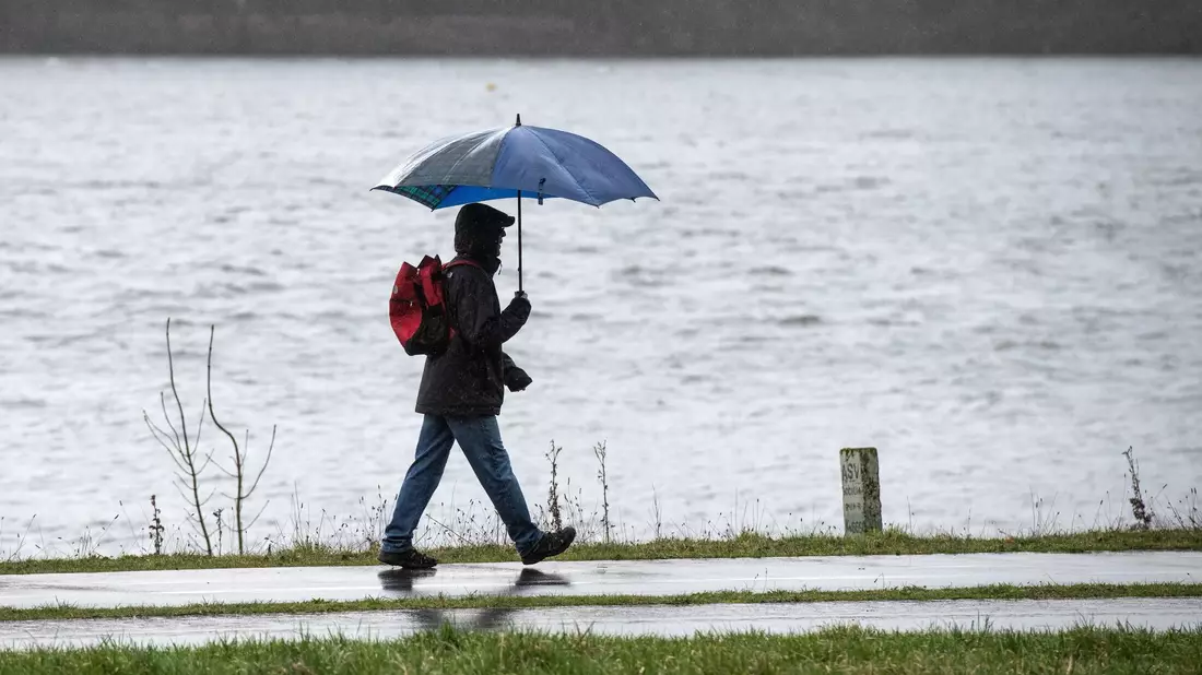Spaziergänger mit Regenschirm am Ufer des Kemnader Sees in Bochum. - Bild: Bernd Thissen/dpa