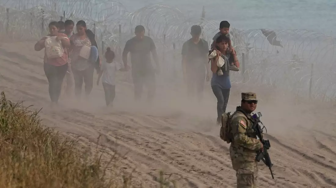 Ein texanischer Wachmann neben Menschen, die den Rio Grande von Mexiko aus in die USA überquert haben. - Bild: Eric Gay/AP