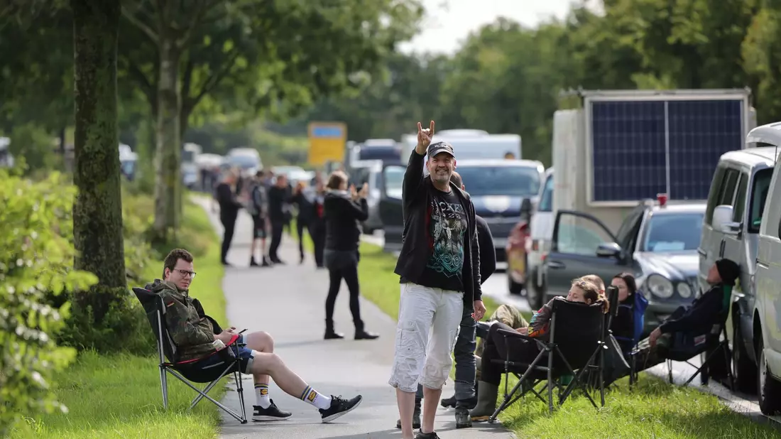 Metal-Fans gehen über das schlammige Festivalgelände. - Bild: Christian Charisius/dpa