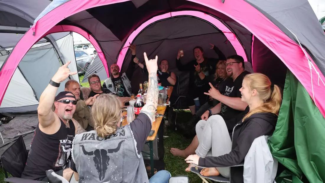 Metal-Fans aus Kiel feiern auf einem Zeltplatz auf dem vom Regen aufgeweichten Festivalgelände. - Bild: Christian Charisius/dpa