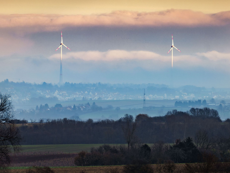 Zwei Windräder ragen aus dem Dunst über der Wetterau heraus. - Foto: Frank Rumpenhorst/dpa