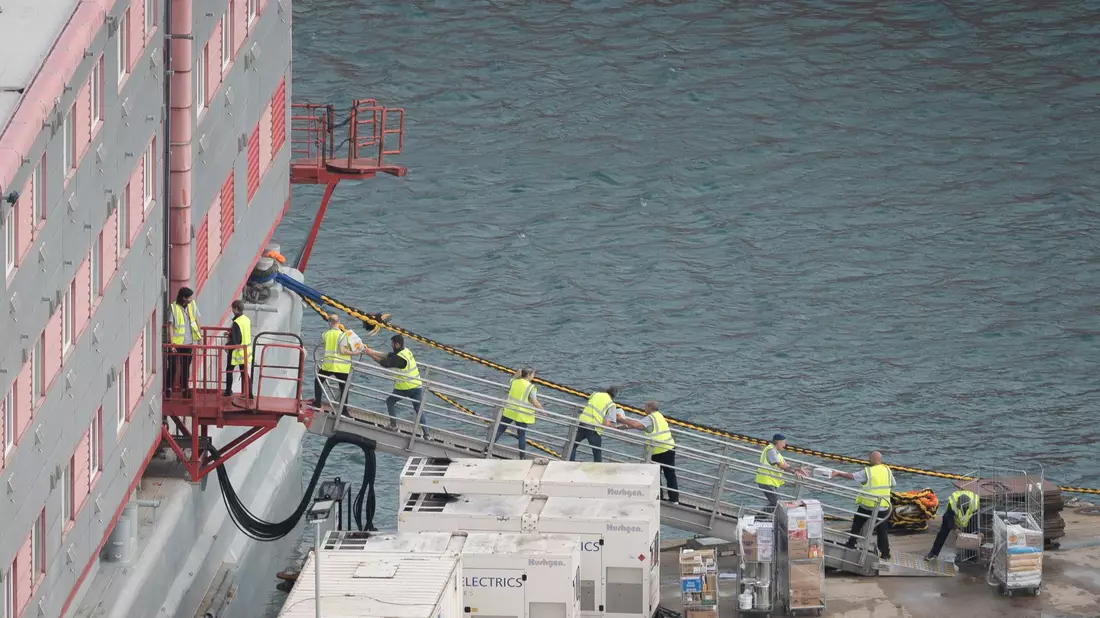 Ein Schleppschiff passiert im Hafen von Portland in Dorset das Schiff «Bibby Stockholm», das bis zu 500 Menschen aufnehmen soll. - Bild: James Manning/PA Wire/dpa