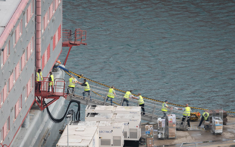 Ein Schleppschiff passiert im Hafen von Portland in Dorset das Schiff «Bibby Stockholm», das bis zu 500 Menschen aufnehmen soll. - Foto: James Manning/PA Wire/dpa Ein Schleppschiff passiert im Hafen von Portland in Dorset das Schiff «Bibby Stockholm», das bis zu 500 Menschen aufnehmen soll. - Foto: James Manning/PA Wire/dpa