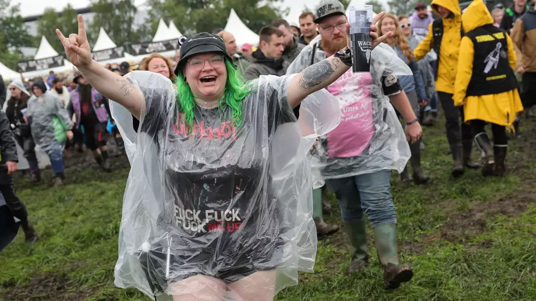 Metal-Fans laufen auf dem nassen Festivalgelände. - Bild: Christian Charisius/dpa