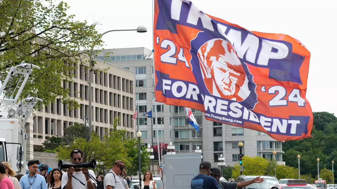 Ein Trump-Unterstützer hat eine riesige Flagge mit zum Gerichtsgebäude in Washington gebracht, wo der Ex-Präsident persönlich erscheinen soll. - Bild: Jacquelyn Martin/AP/dpa