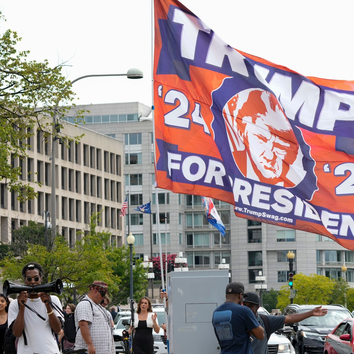 Ein Trump-Unterstützer hat eine riesige Flagge mit zum Gerichtsgebäude in Washington gebracht, wo der Ex-Präsident persönlich erscheinen soll. - Foto: Jacquelyn Martin/AP/dpa
