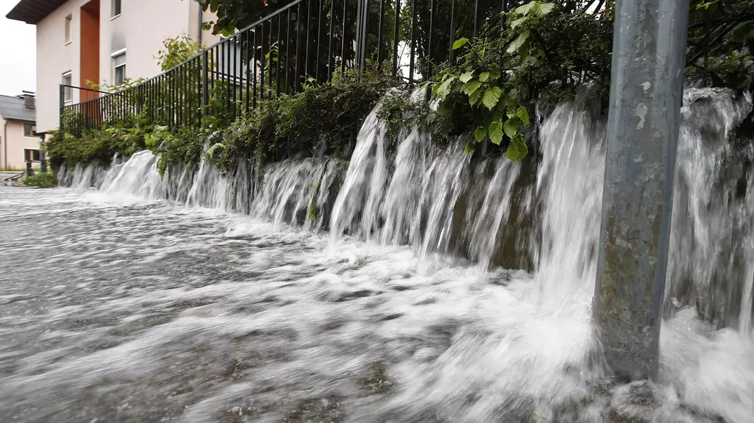 Wasser strömt auf eine Straße in Viktring bei Klagenfurt in Kärnten. - Bild: Gerd Eggenberger/APA/dpa