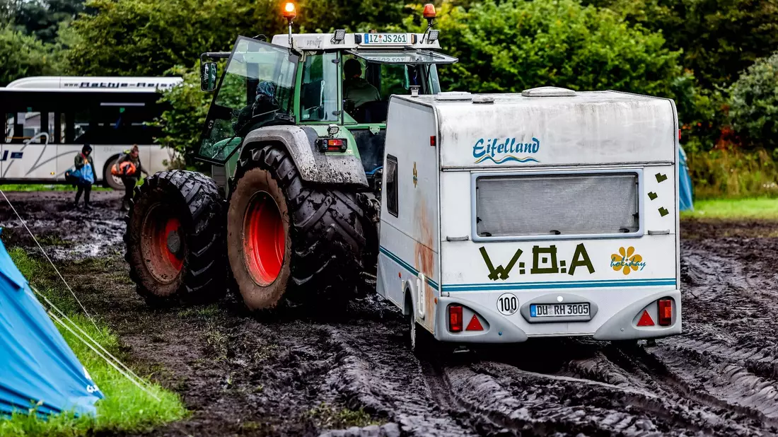 Ab durch den Schlamm: Ein Traktor zieht einen Wohnwagen vom Campinggelände des Wacken Open Air. - Bild: Axel Heimken/dpa