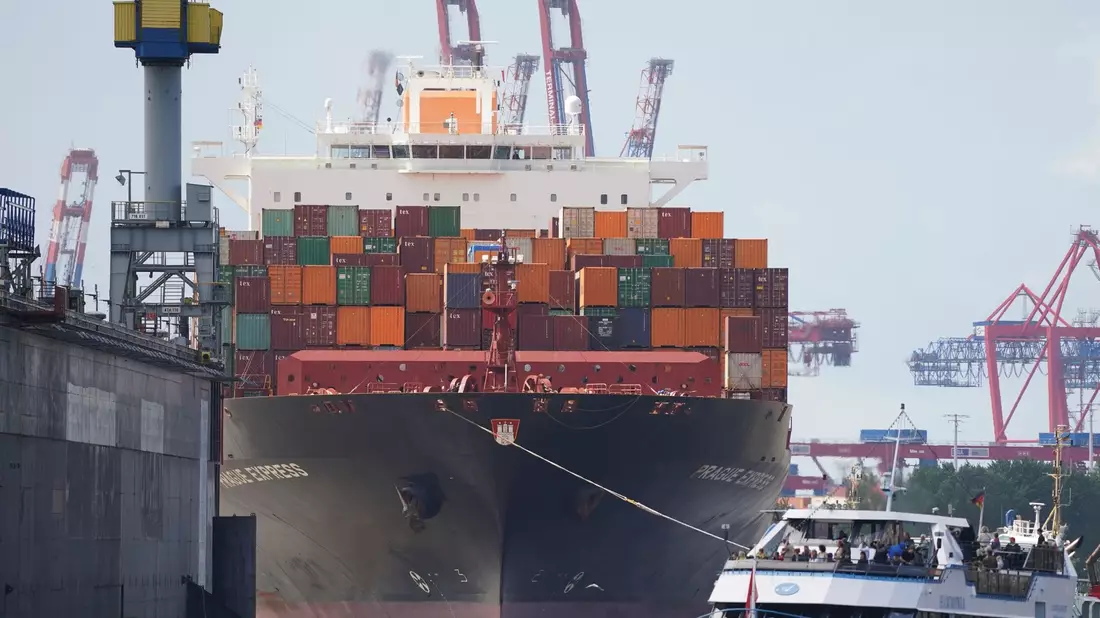 Das Containerschiff «Prague Express» der Reederei Hapag-Lloyd wird von Schleppern an einen Containerterminal im Hafen gezogen. - Bild: Marcus Brandt/dpa