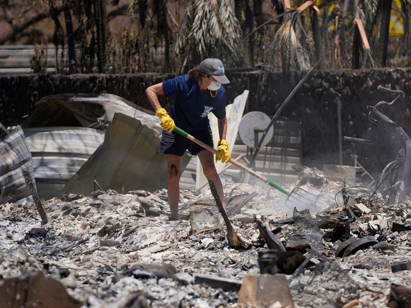 Eine Frau gräbt in Lahaina auf Hawaii in den Trümmern eines zerstörten Hauses. - Foto: Rick Bowmer/AP/dpa