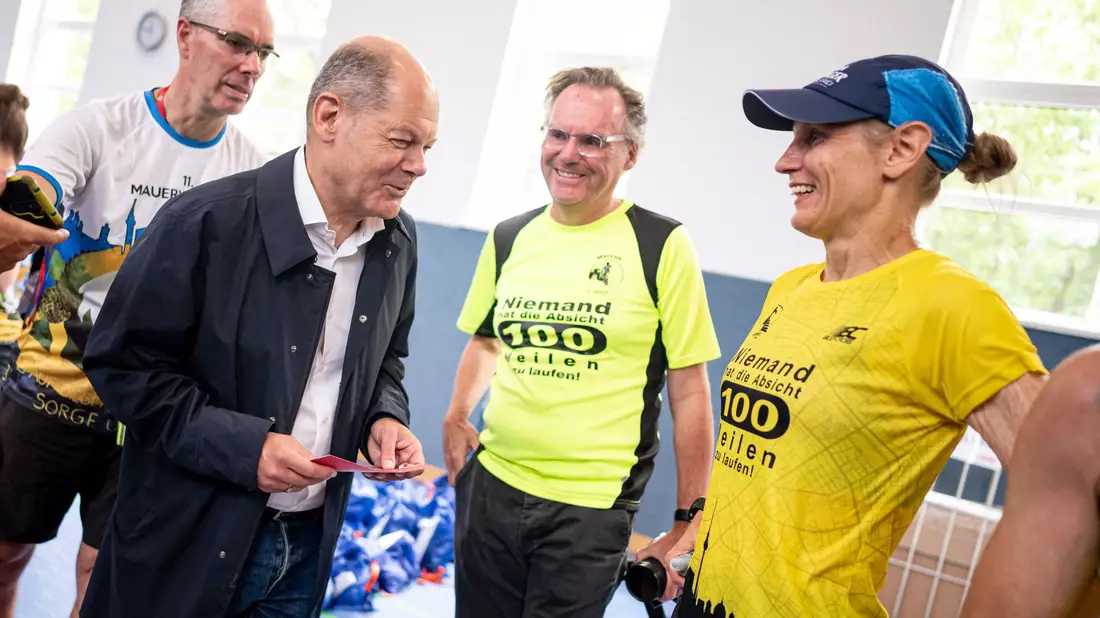 Entspannter Besuch: Scholz unterhält sich mit Läuferinnen und Läufern beim Berliner Mauerweglauf. - Bild: Fabian Sommer/dpa