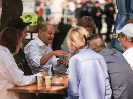 Bundeskanzler Olaf Scholz (M, SPD) spricht vor einem Büdchen mit Düsseldorfer Bürgern. - Foto: Oliver Berg/dpa