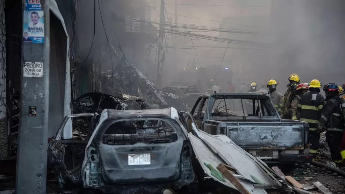 Feuerwehrleute arbeiten neben zerstörten Fahrzeugen nach einer starken Explosion, die ein Marktviertel mit vielen Geschäften erschüttert hat. - Bild: Jolivel Brito/AP/dpa