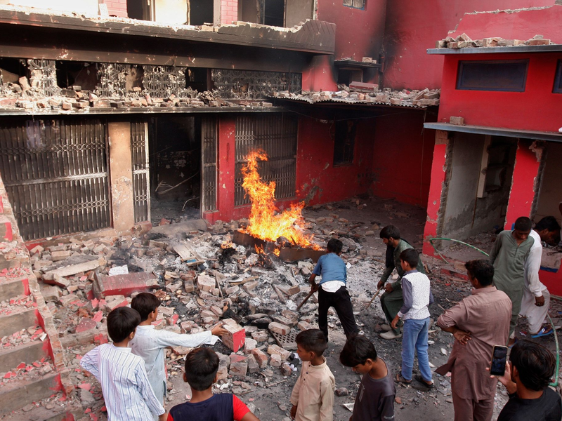 Jugendliche stehen in Jaranwala vor einer Kirche, die beschädigt und niedergebrannt wurde. - Foto: Muhammad Shafqat/AP/dpa