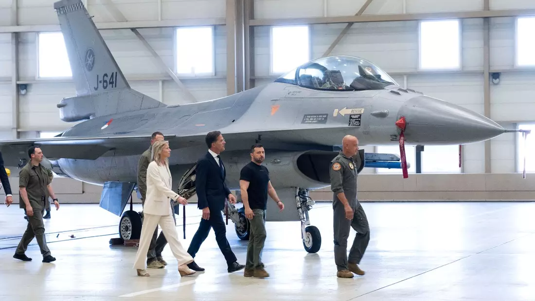 Wolodymyr Selenskyj (2.v.r) und Mark Rutte (M) laufen an einem F-16 Kampfjet vorbei. - Bild: Peter Dejong/AP/dpa