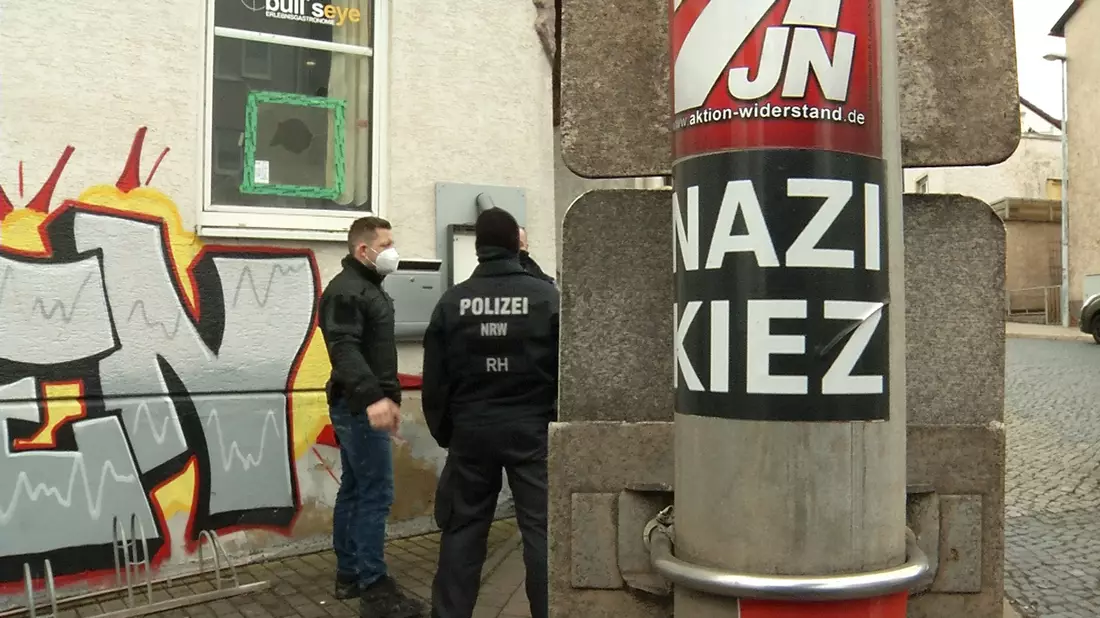 Polizisten stehen vor der Gaststätte «Bull's Eye». An einem Pfahl ist ein Aufkleber mit der Aufschrift «Nazi Kiez» zu sehen. - Bild: Martin Wichmann TV/dpa