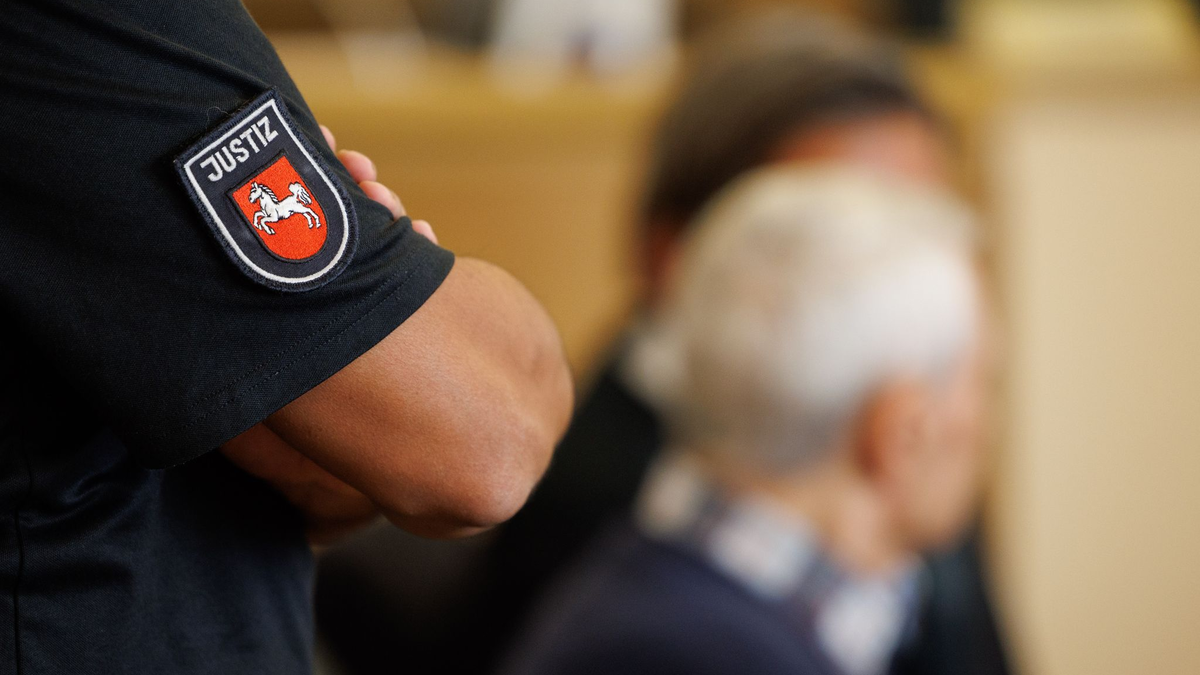 Ein Justizbeamter steht hinter dem Angeklagten im Saal des Landgerichts Osnabrück. - Foto: Friso Gentsch/dpa