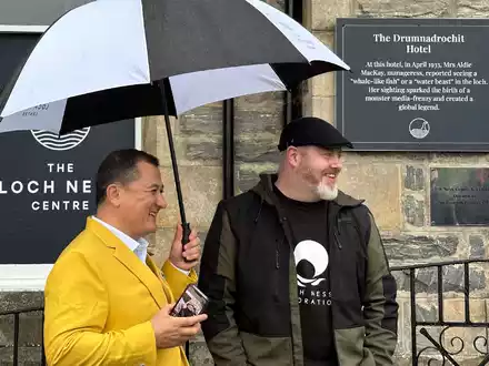 Paul Nixon (l) vom Loch Ness Centre und der Projektleiter Alan McKenna neben der Plakette, die an eine berühmte Nessie-Sichtung im Jahr 1933 erinnert. - Foto: Benedikt von Imhoff/dpa