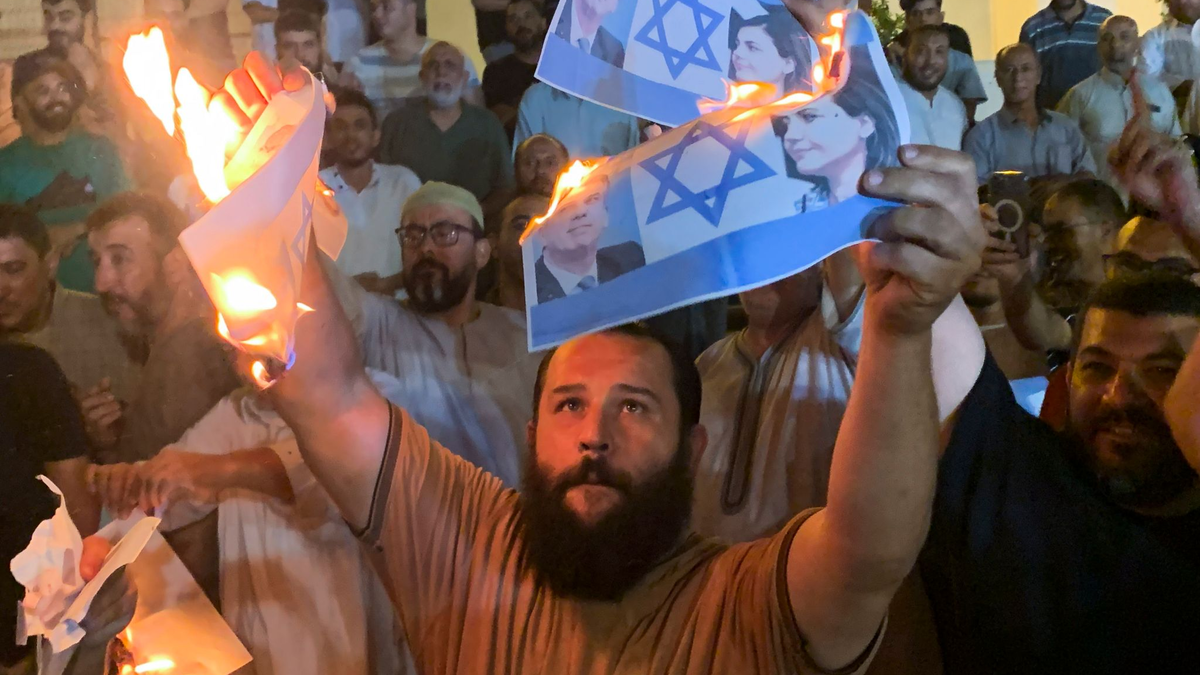 Menschen verbrennen in Tripolis Bilder, die den israelischen Außenminister Eli Cohen und seine libysche Amtskollegin Nadschla al-Mankusch zeigen. - Foto: Yousef Murad/AP