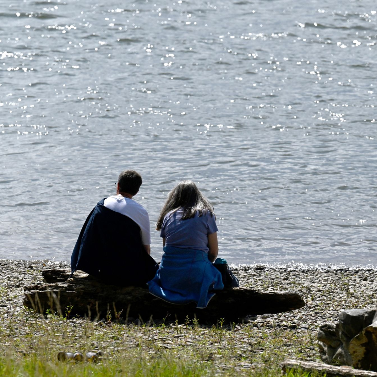 Spaziergänger sitzen am Ufer des Rheins und genießen die Sonne. - Foto: Roberto Pfeil/dpa
