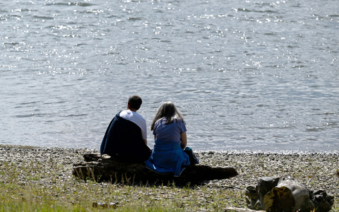 Spaziergänger sitzen am Ufer des Rheins und genießen die Sonne. - Foto: Roberto Pfeil/dpa