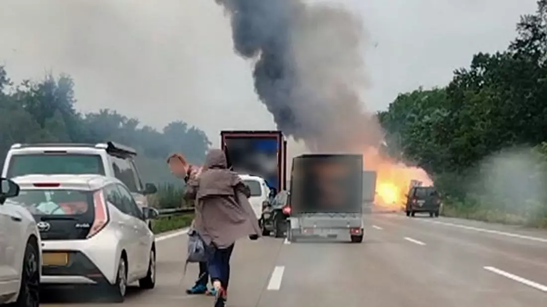 Autofahrer verlassen ihre Fahrzeuge, während im Hintergrund ein Lkw in Flammen steht. Nach einem Auffahrunfall sind auf einem Gefahrguttransporter mehrere Gasflaschen explodiert. - Bild: -/TNN/dpa