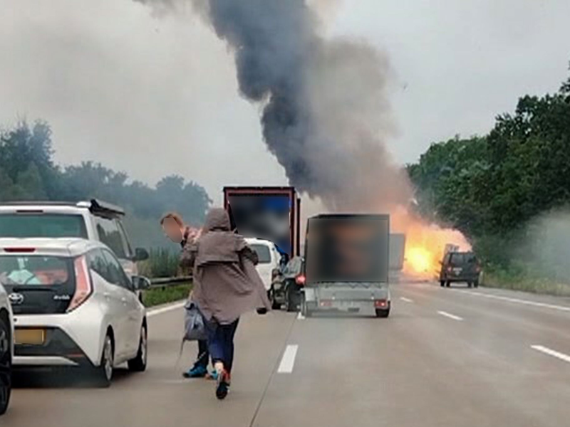 Autofahrer verlassen ihre Fahrzeuge, während im Hintergrund ein Lkw in Flammen steht. Nach einem Auffahrunfall sind auf einem Gefahrguttransporter mehrere Gasflaschen explodiert. - Foto: -/TNN/dpa