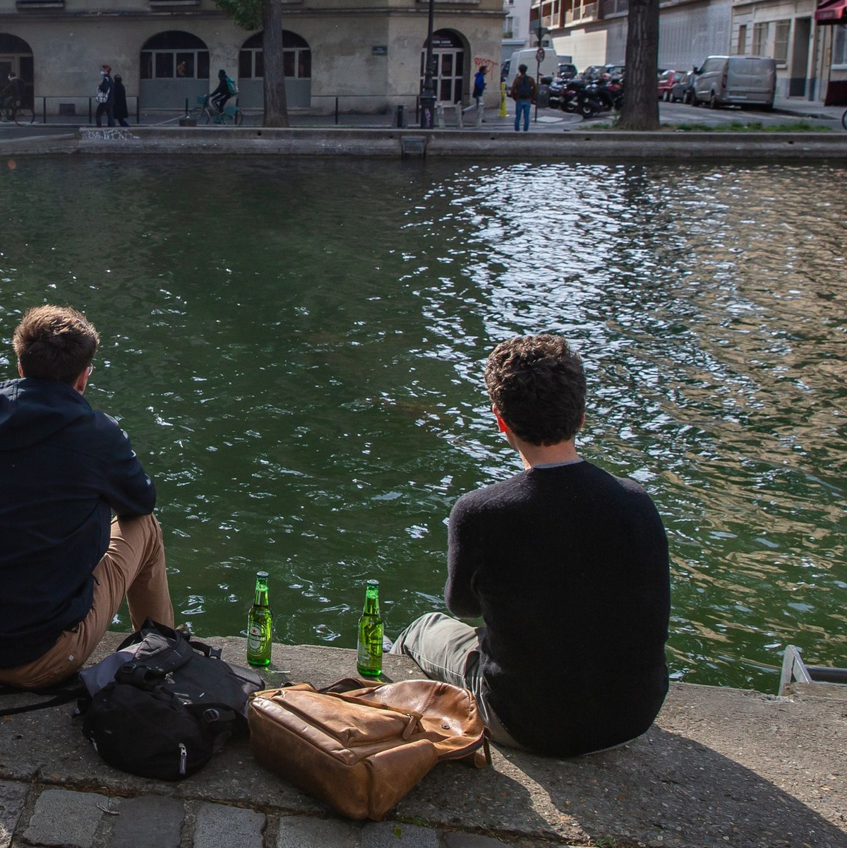 Zwei junge Männer trinken am Ufer des Kanals Saint-Martin in Paris gemeinsam Bier. - Foto: Aurelien Morissard/XinHua/dpa