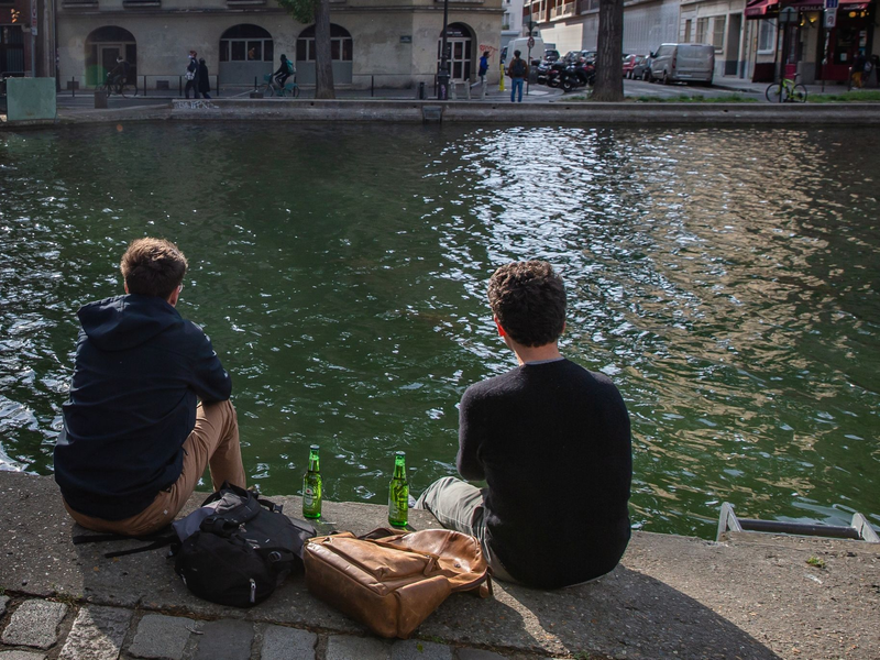 Zwei junge Männer trinken am Ufer des Kanals Saint-Martin in Paris gemeinsam Bier. - Foto: Aurelien Morissard/XinHua/dpa