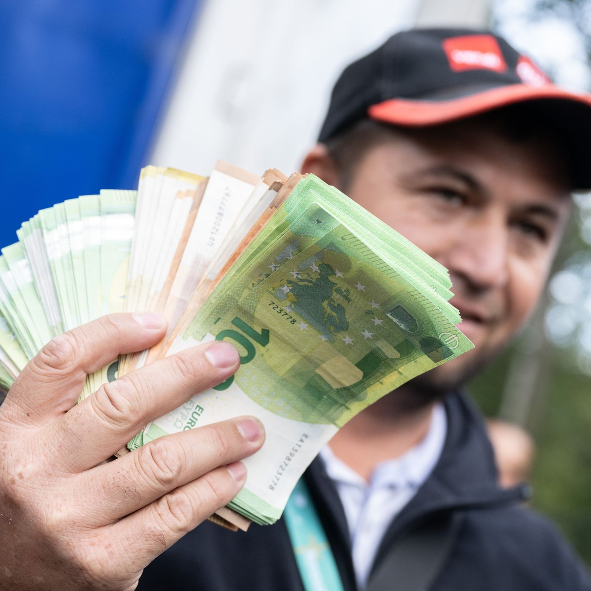 Ein Lkw-Fahrer mit einem Bündel Geldscheinen in der Hand. - Foto: Boris Roessler/dpa