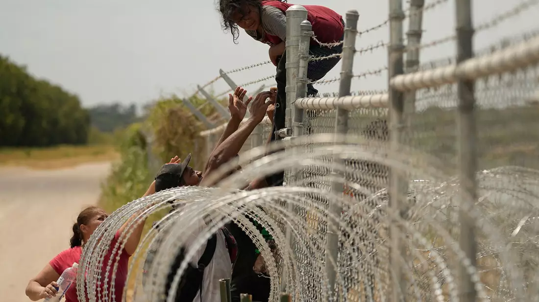 Migranten, die den Rio Grande von Mexiko in die USA überquert haben, klettern in Texas über einen Zaun mit Stacheldraht. - Bild: Eric Gay/AP