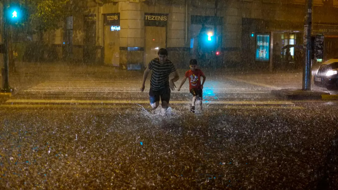 Menschen überqueren bei starkem Regen eine überschwemmte Straße in Pamplona. - Bild: Alvaro Barrientos/AP