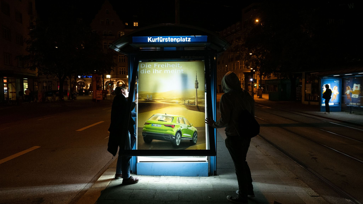 Aktivisten von Attac bringen als Protest gegen die IAA kritische Persiflagen von Autowerbung an einem Trambahnhäuschen an. - Foto: Lukas Barth/dpa