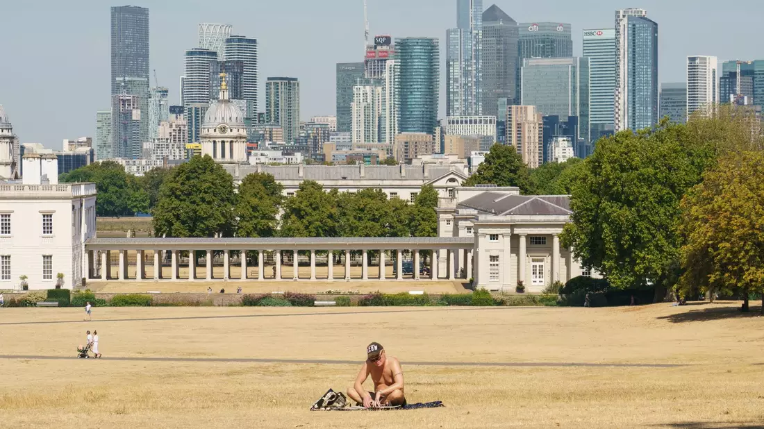 Ein Mann sonnt sich auf vertrocknetem Gras im Greenwich Park, im Hintergrund die Skyline von London (2022). - Bild: Dominic Lipinski/PA Wire/dpa