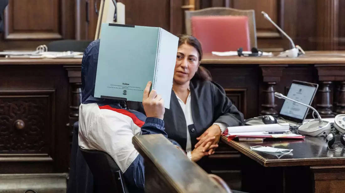 Der Angeklagte verbirgt zu Prozessbeginn sein Gesicht hinter einem Aktenordner. Er soll seine im Rollstuhl sitzende Großmutter getötet haben. - Bild: Markus Scholz/dpa