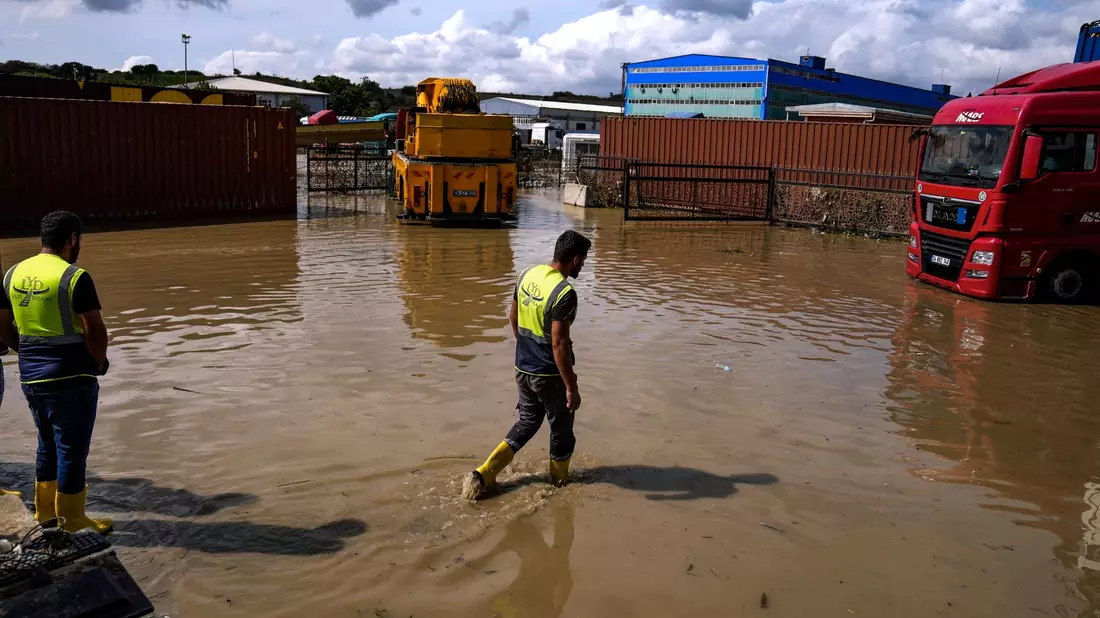 Arbeiter laufen nach Überschwemmungen durch schwere Regenfälle durch das Hochwasser. - Bild: Khalil Hamra/AP/dpa