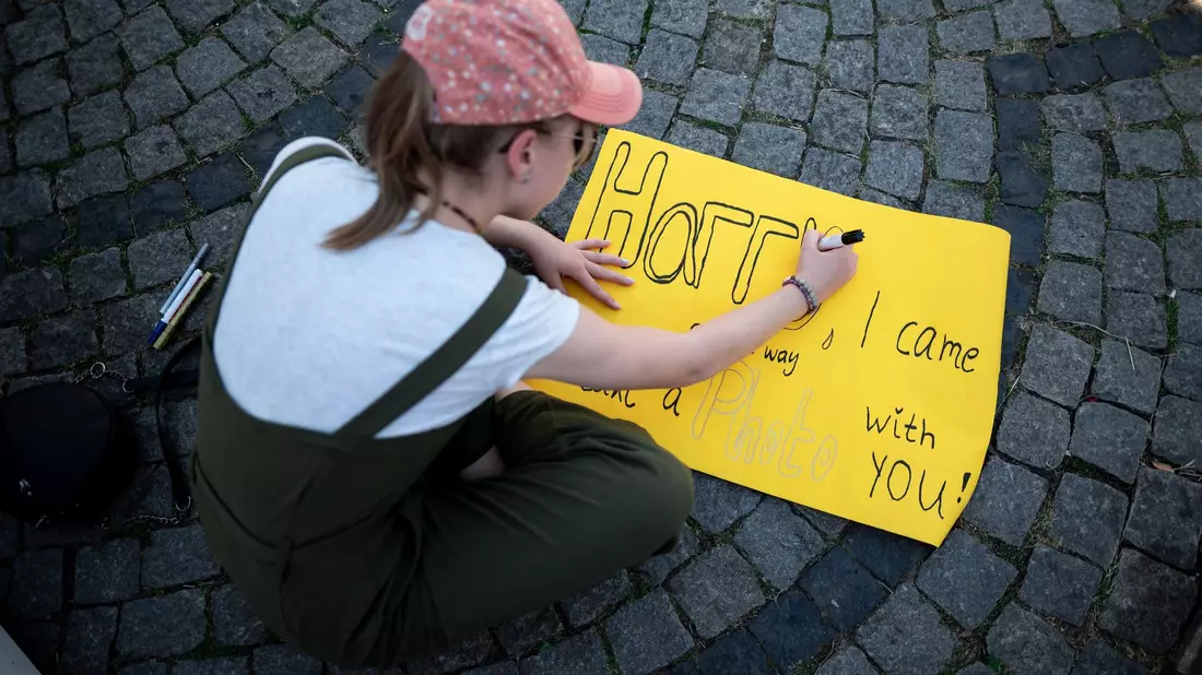Eine junge Frau schreibt auf ein Schild: «Harry, I came all the way to take a photo with you!» - Bild: Fabian Strauch/dpa