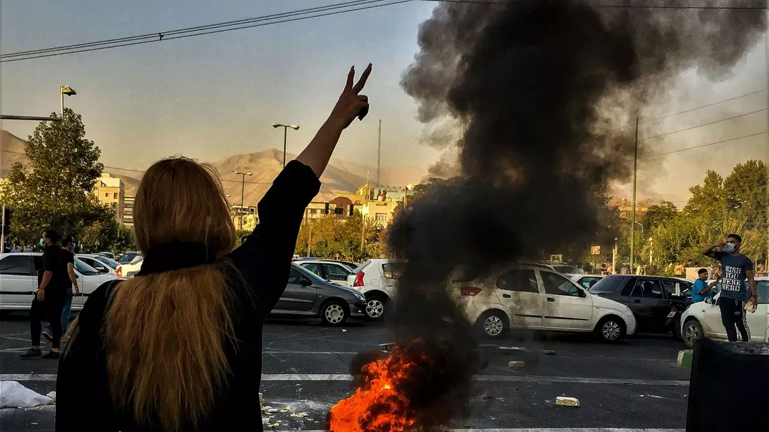 Eine Frau steht während einer Demonstration in Teheran vor einem brennenden Autoreifen und zeigt das Victory-Zeichen. - Bild: Uncredited/AP/dpa