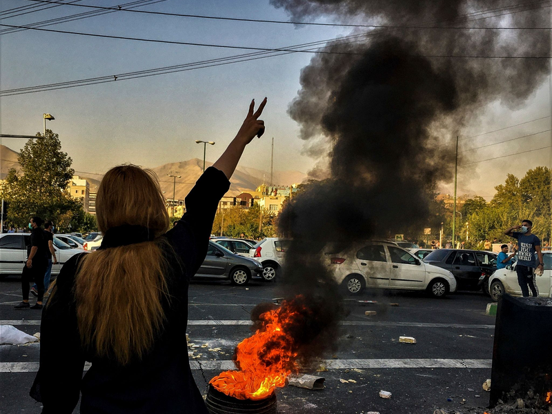 Eine Frau steht während einer Demonstration in Teheran vor einem brennenden Autoreifen und zeigt das Victory-Zeichen. - Foto: Uncredited/AP/dpa