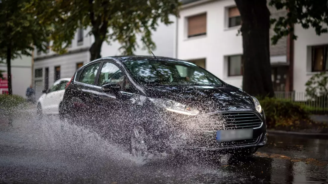 Nach starken Regenfällen am Dienstagmorgen fährt ein Auto durch eine große Pfütze in Duisburg. - Bild: Christoph Reichwein/dpa
