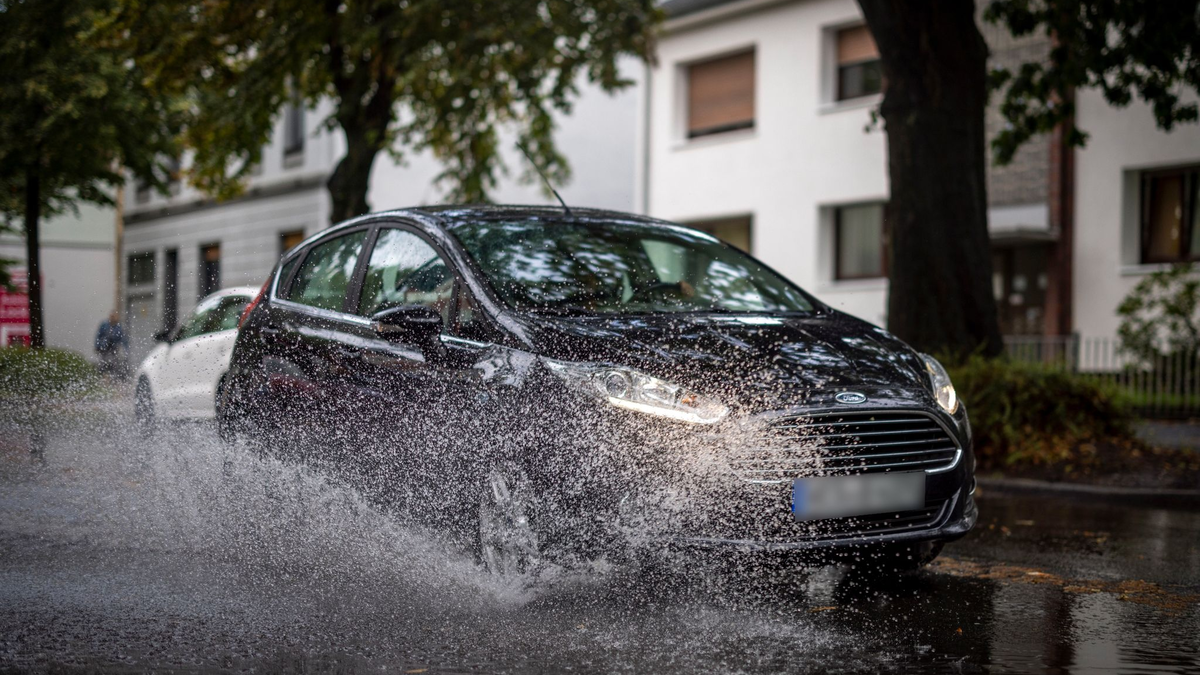 Nach starken Regenfällen am Dienstagmorgen fährt ein Auto durch eine große Pfütze in Duisburg. - Foto: Christoph Reichwein/dpa