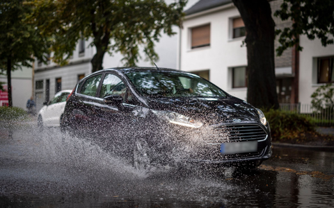 Nach starken Regenfällen am Dienstagmorgen fährt ein Auto durch eine große Pfütze in Duisburg. - Foto: Christoph Reichwein/dpa