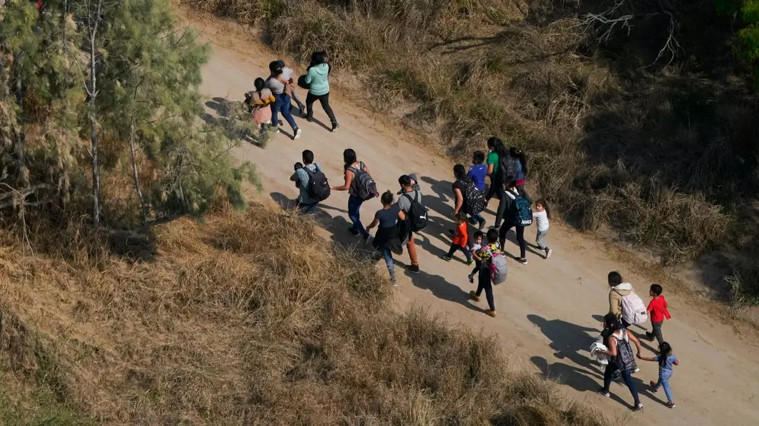 Migranten gehen einen Feldweg entlang, nachdem sie die Grenze zwischen den USA und Mexiko überquert haben. - Bild: Julio Cortez/AP/dpa