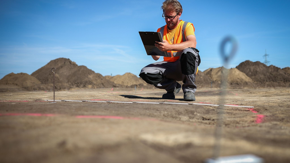 Der Archäologe Nikita Sirman vom Landesamt für Denkmalpflege und Archäologie vermisst und kartiert den mutmaßlichen Grundriss eines Grubenhauses. - Foto: Ronny Hartmann/dpa