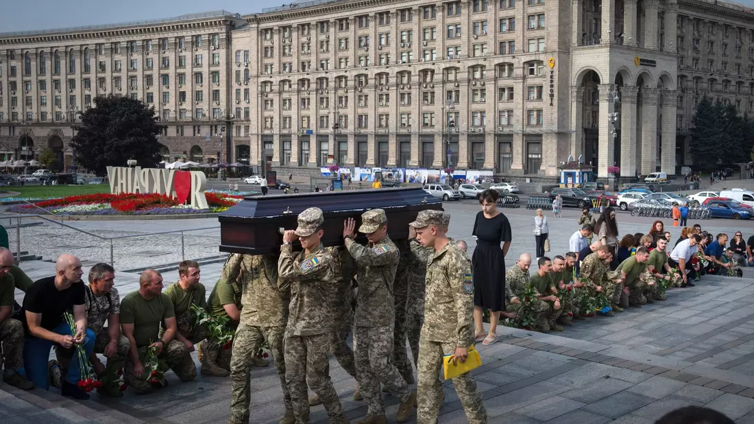 Menschen in Kiew knien nieder, während Soldaten den Sarg eines Kameraden tragen, der in einem Gefecht getötet wurde. - Bild: Efrem Lukatsky/AP/dpa