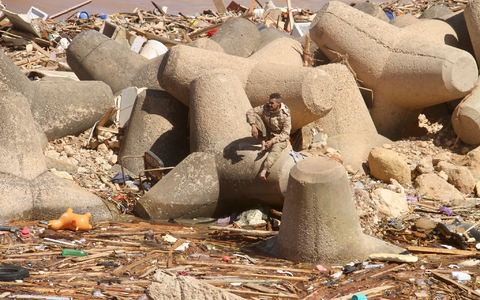 Ein Mann sitzt auf einem Wellenbrecher und blickt auf einen Teil der Schäden. - Foto: Yousef Murad/AP/dpa